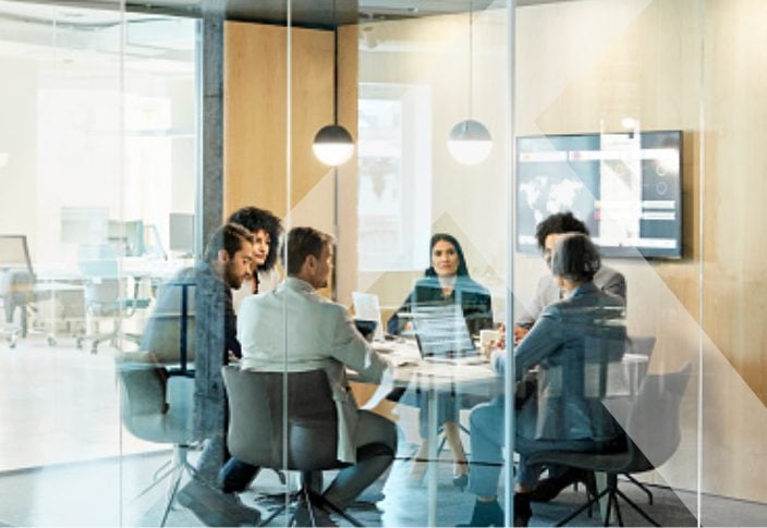 Small business employees with laptops on table meet in a glass-walled conference room