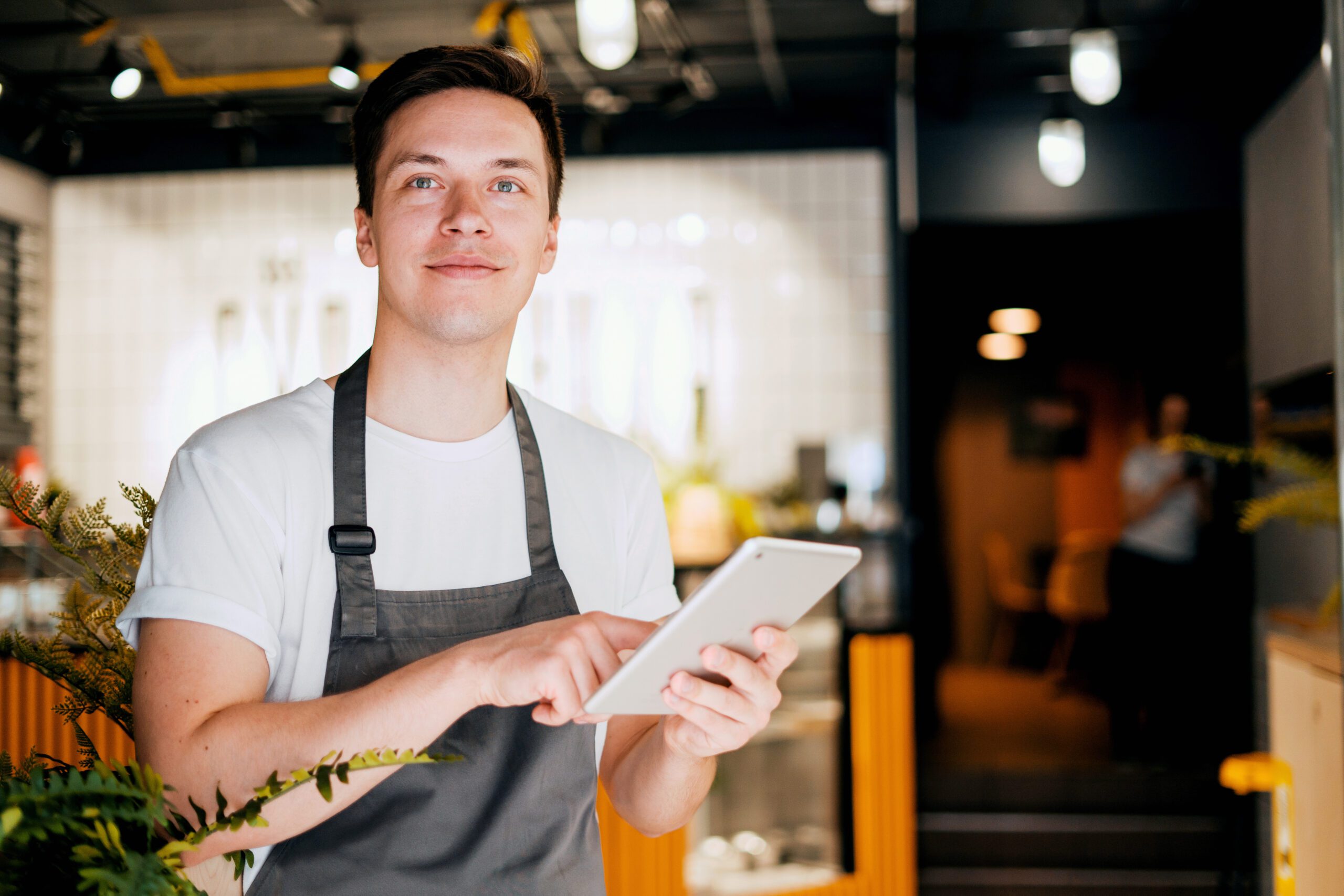 A male employee in an apron is working on a tablet in a restaurant powered by business-class WIFI by Kinetic Business
