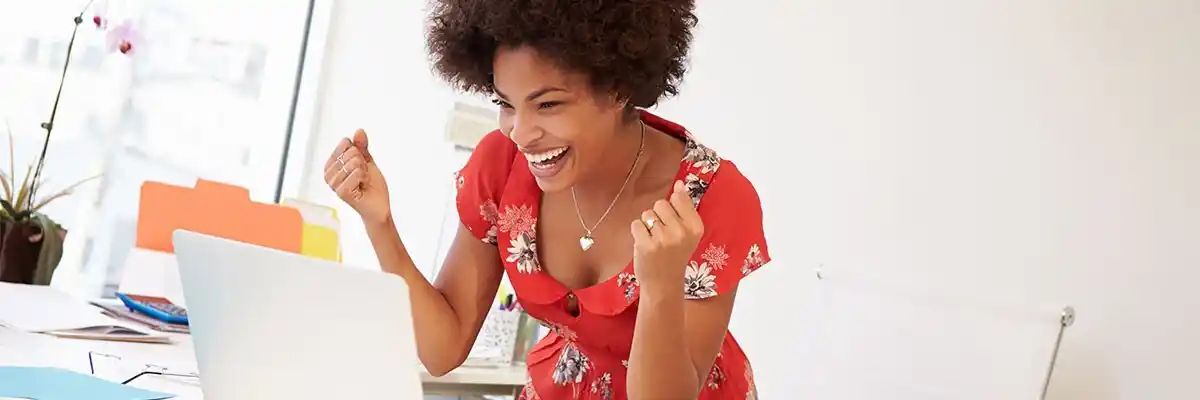 Black businesswoman celebrates with double fist pumps in front of her laptop