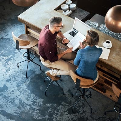 Man and woman working together in shared space with a laptop and other wireless devices.