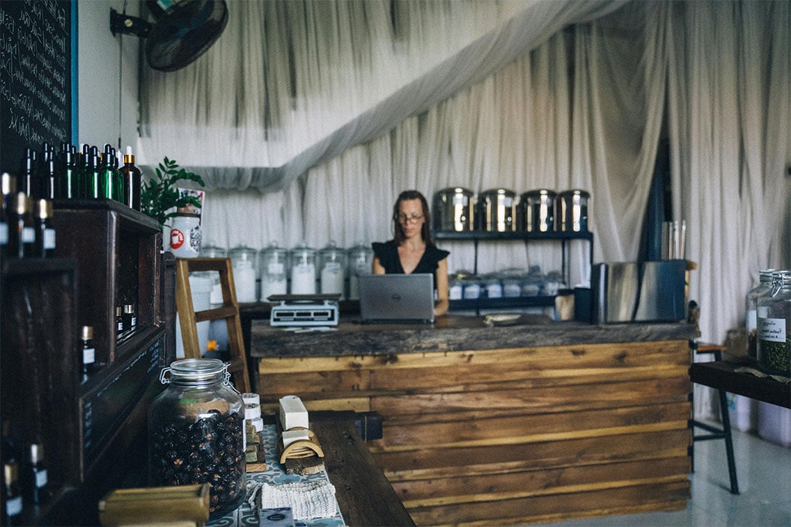 Coffee shop manager using a connected device behind the counter of shop with product displayed.